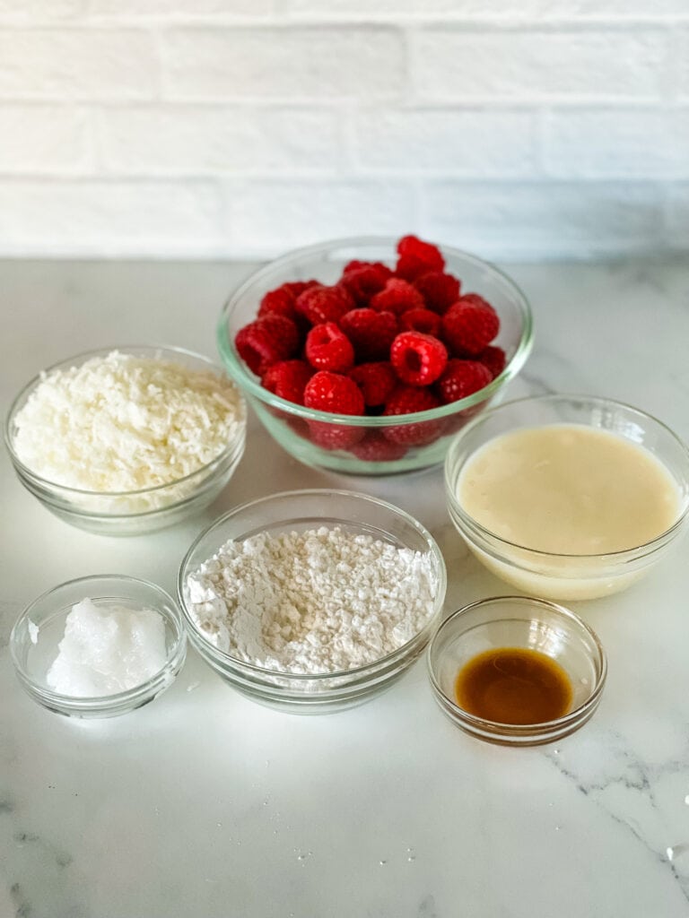 Ingredients needed for raspberry coconut truffles. Including coconut, fresh raspberries, coconut oil, powdered sugar, vanilla, and coconut butter.