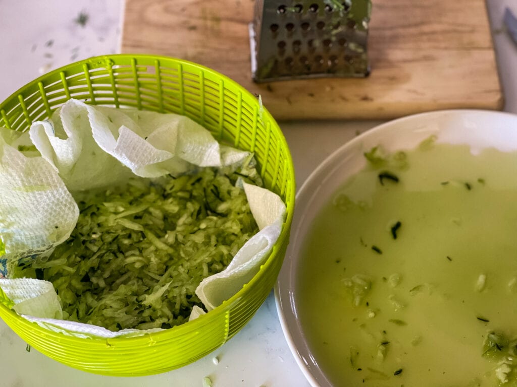 on the left a green strainer with shredded cucumber on a papertowel and on the right a plate showing all the water that is in the shredded cucumber