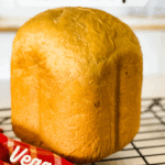 loaf of baked vegan white bread machine bread on wire rack with red checkered napkin with pinterest text overlay