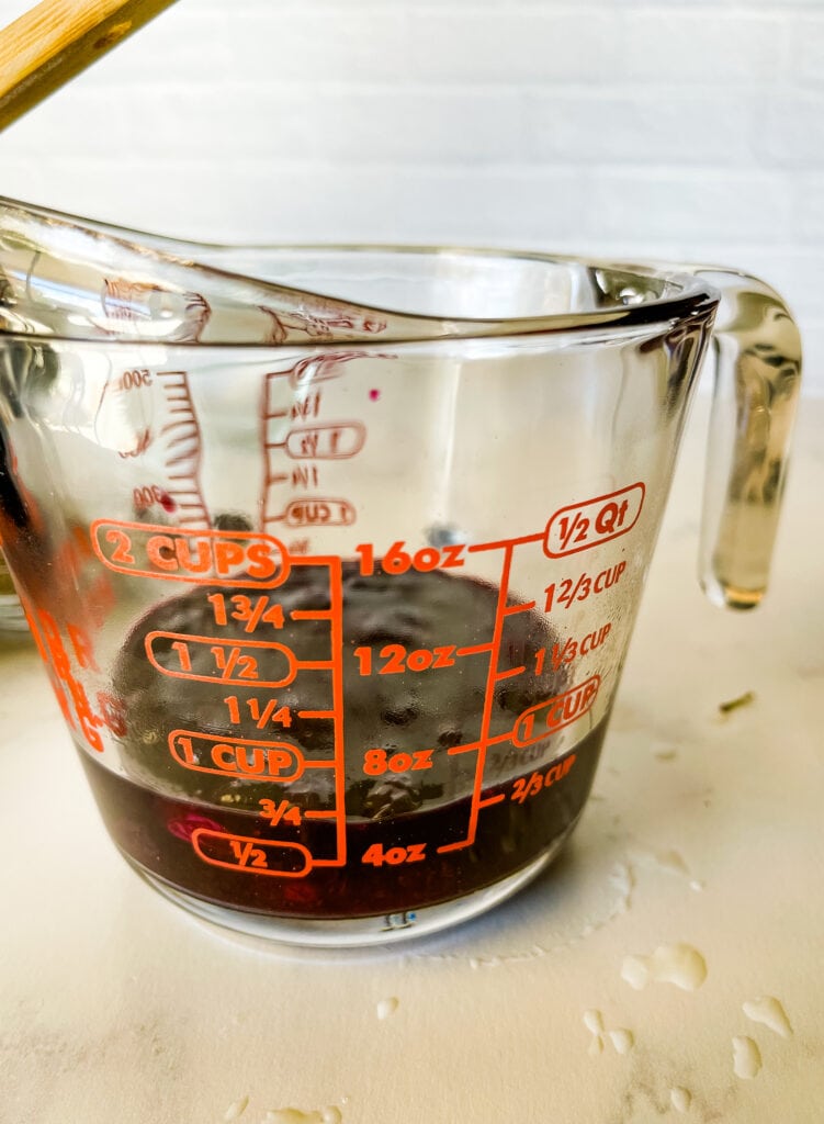 showing the cooked jam in the measuring cup measuring between three quarters and two thirds a cup