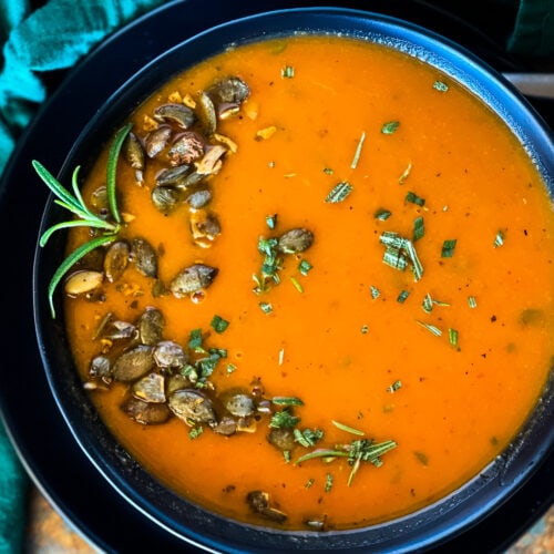 bowl of butternut squash red pepper soup with pepitas and rosemary garnish