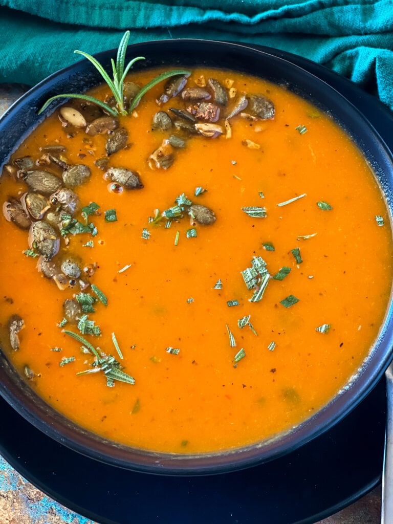bowl of butternut squash red pepper soup with pepitas and rosemary garnish