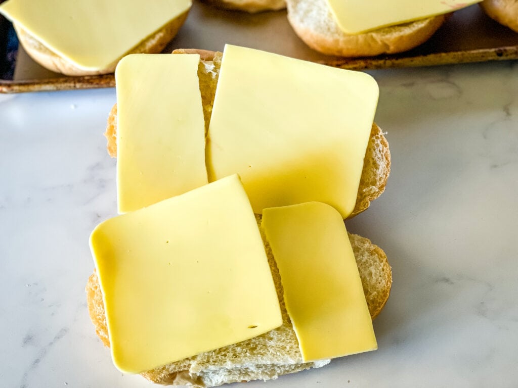 Adding cheese to buns for grinder sandwiches.