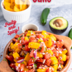 Mango Pico de Gallo in a bowl in front with chips, jalapeno pepper, and half an avocado in the background with pinterest text overlay