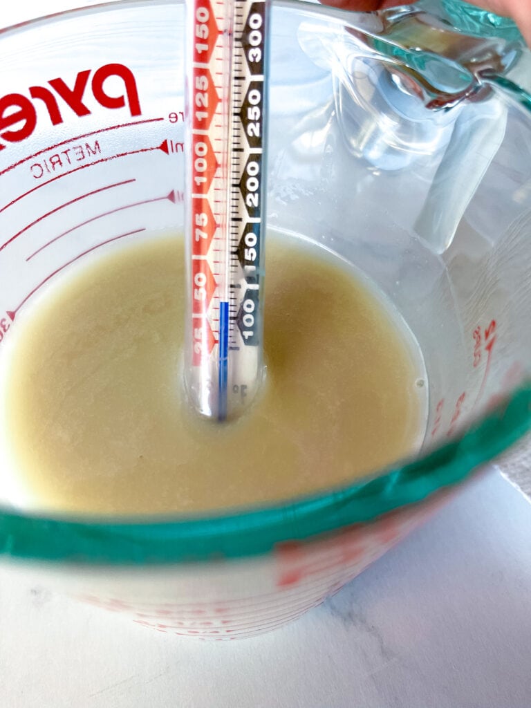 Thermometer in glass measuring cup with warmed oatmilk. Thermometer showing 110 degrees F.