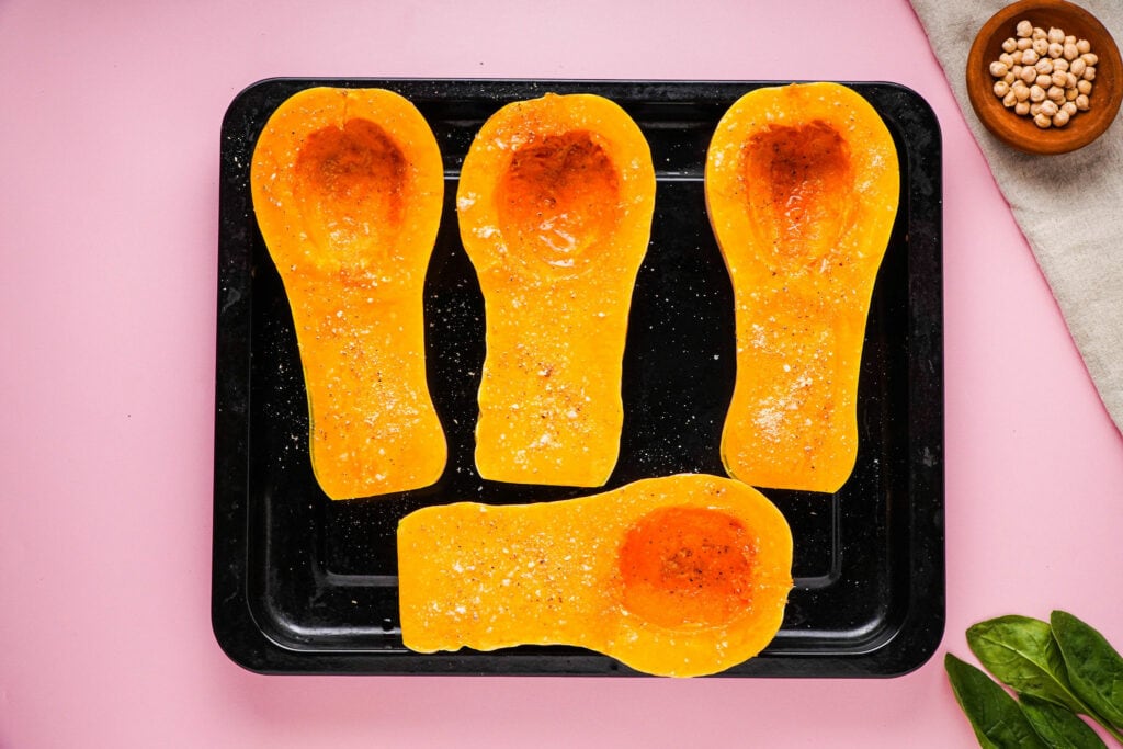 Four oiled and seasoned butternut squash halves ready for roasting.