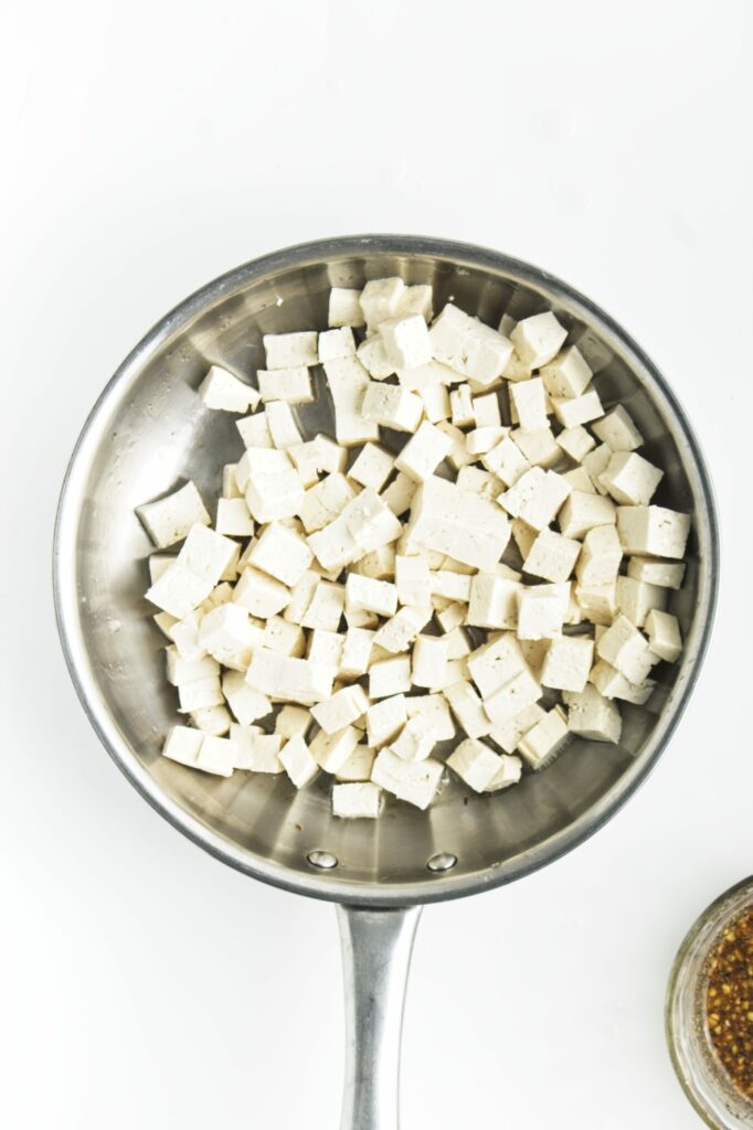 A pan of drained, pressed, and cubed firm tofu. The tofu has started to cook.