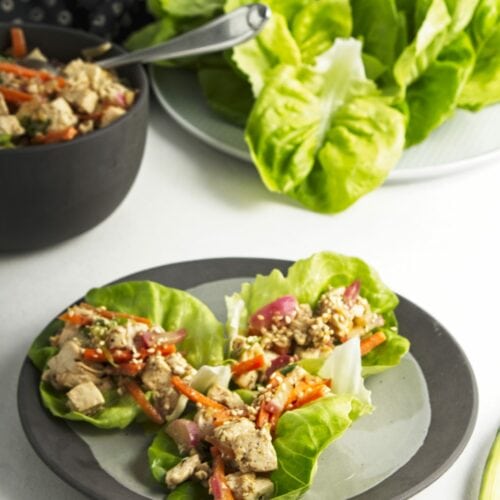 A small plate with three prepared tofu lettuce wraps with a bowl of the tofu mixture and a plate of butter lettuce in the background