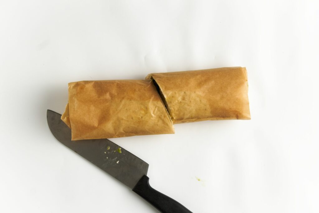 Cutting a lavish wrapped tofu wrap. The wrap is in parchment paper.