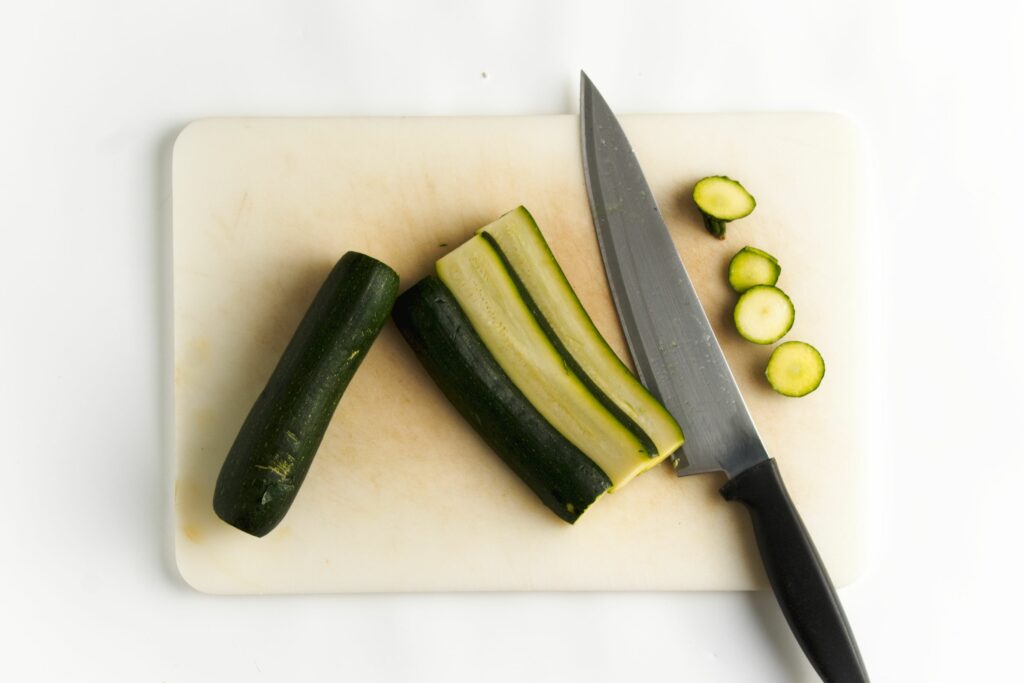 Cutting the zucchini into three lengthwise sliced each. The zucchini on the left is not cut next to a sliced zucchini on the right. Then is a knife and the zucchini tops and bottoms.