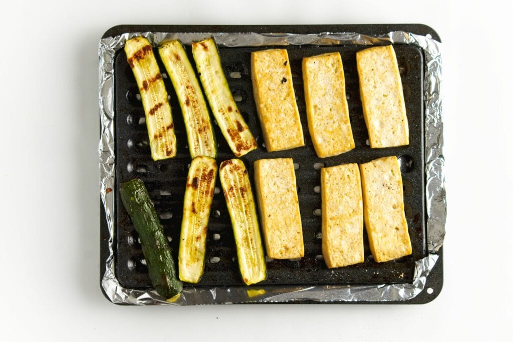 six slices of zucchini and six sliced of tofu baked on a grilling pan after having spent a few minutes under the broiler.