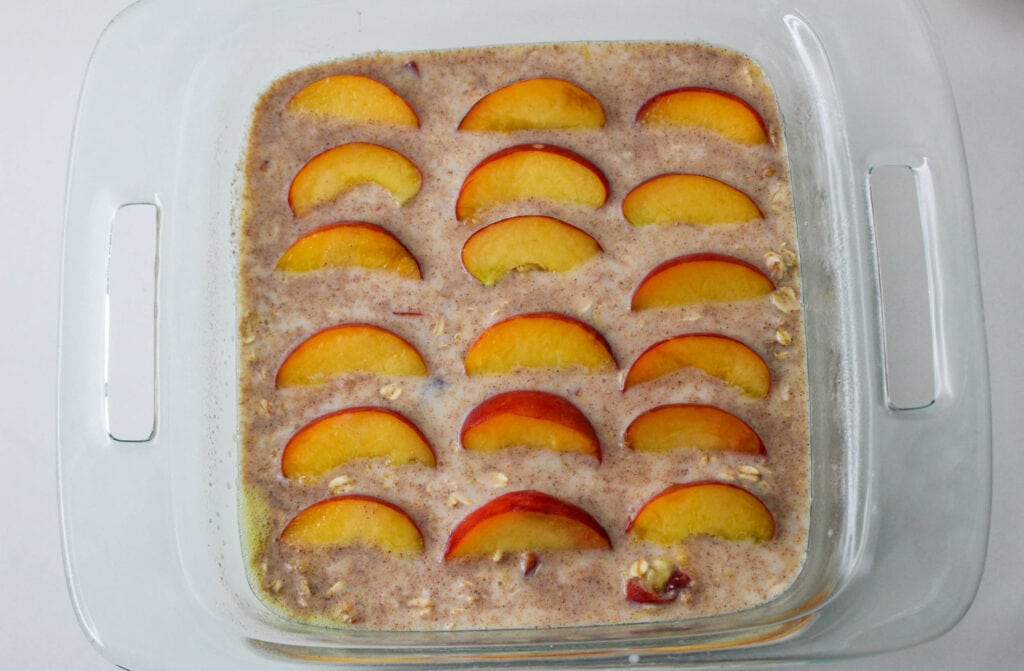 unbaked peach oatmeal in a casserole dish with sliced peaches on top.