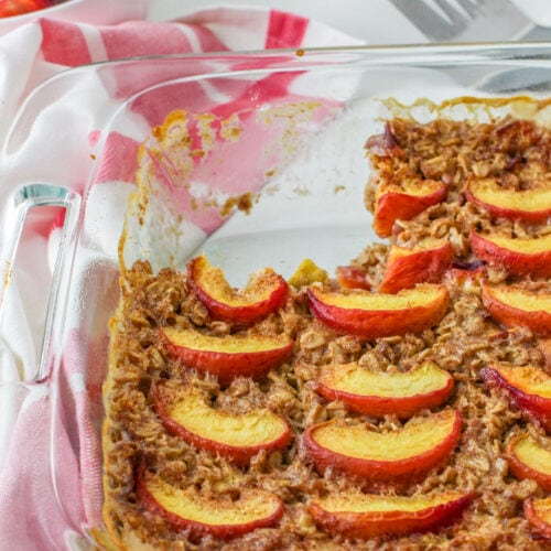 Baked peach oats in a glass baking dish with a piece removed.