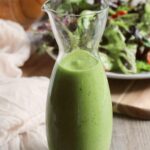 Jar of green goddess dressing in the front with a salad in the background.