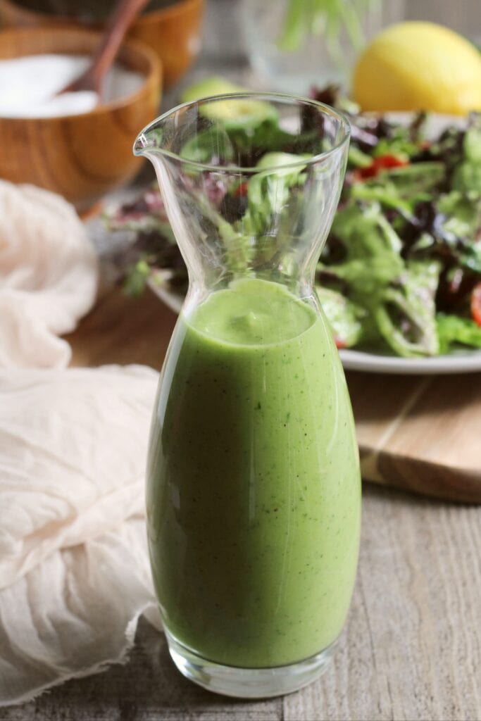 Jar of green goddess dressing in the front with a salad in the background.