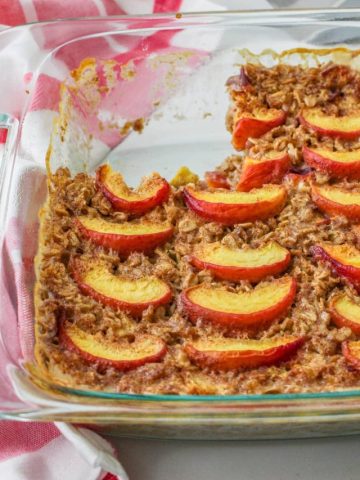 Baked peach oats in a glass baking dish with a piece removed.