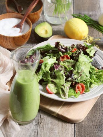 Jar of green goddess dressing in the front with a salad in the background.