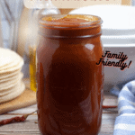 A jar of enchilada sauce with tortillas and white bowls in the background with pinterest overlay text.