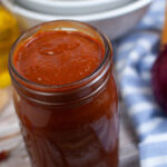 A jar of enchilada sauce with a blue striped cloth and white bowls in the background.