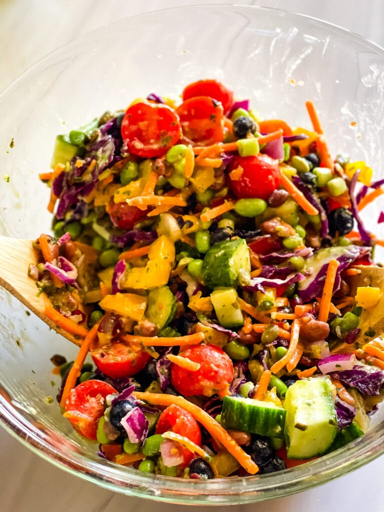 Tossing the rainbow salad along with the dressing in a larger glass mixing bowl.
