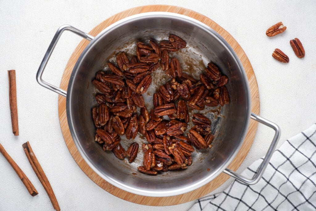The pecans in the saucepan tossed with the melted ingredients.