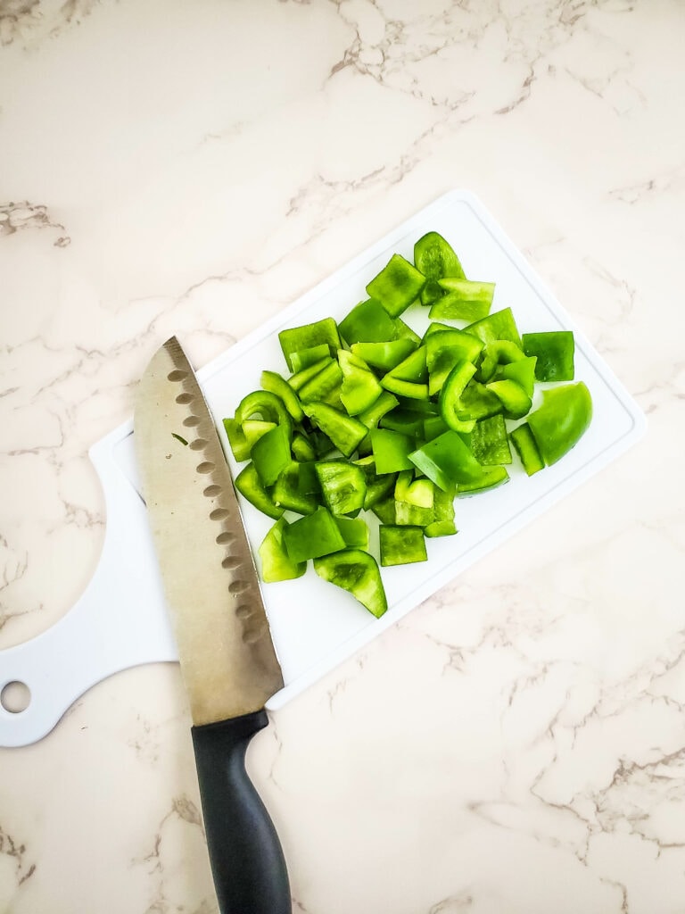 White chopping board with a knife and green peppers.