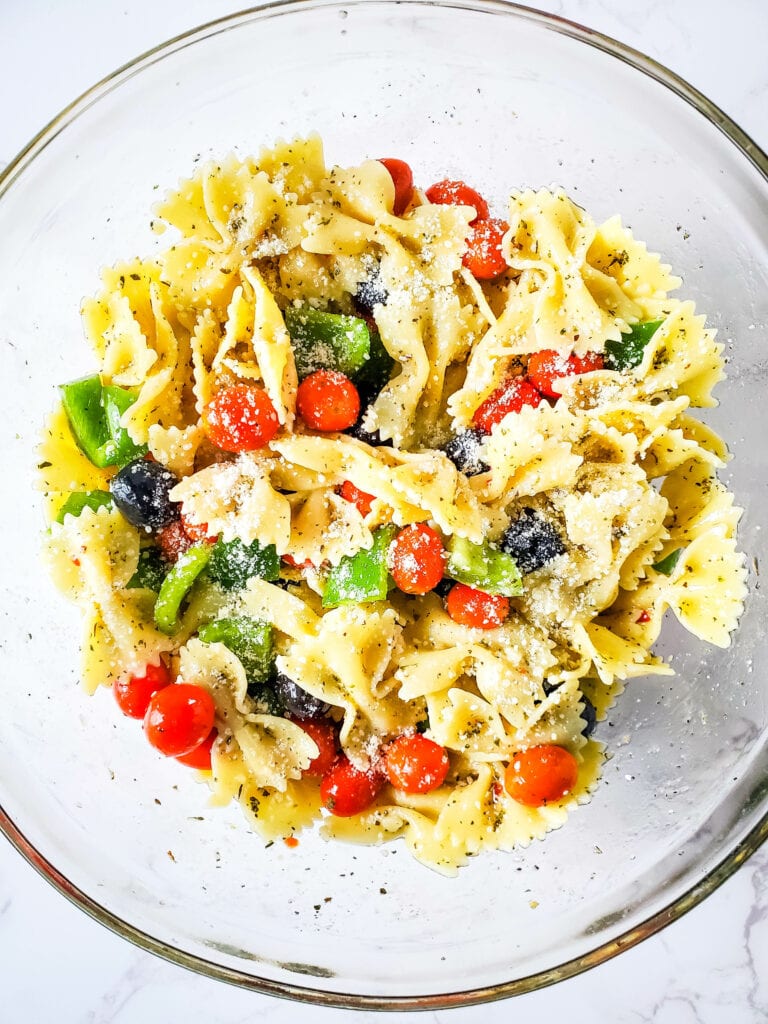 The bow tie pasta salad all mixed together in the glass bowl with an extra sprinkling of vegan parm on top.