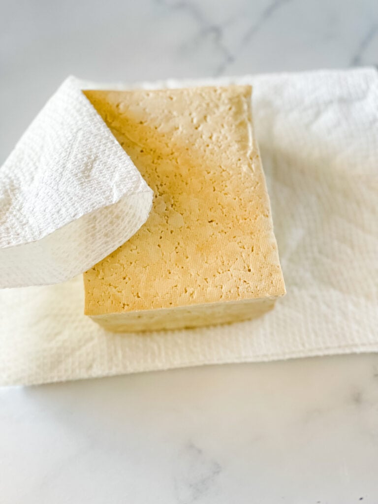 Patting the pressed tofu dry with a paper towel.