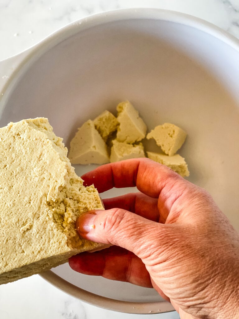 Breaking apart the pressed tofu by hand into small chunks and putting them in a white bowl.