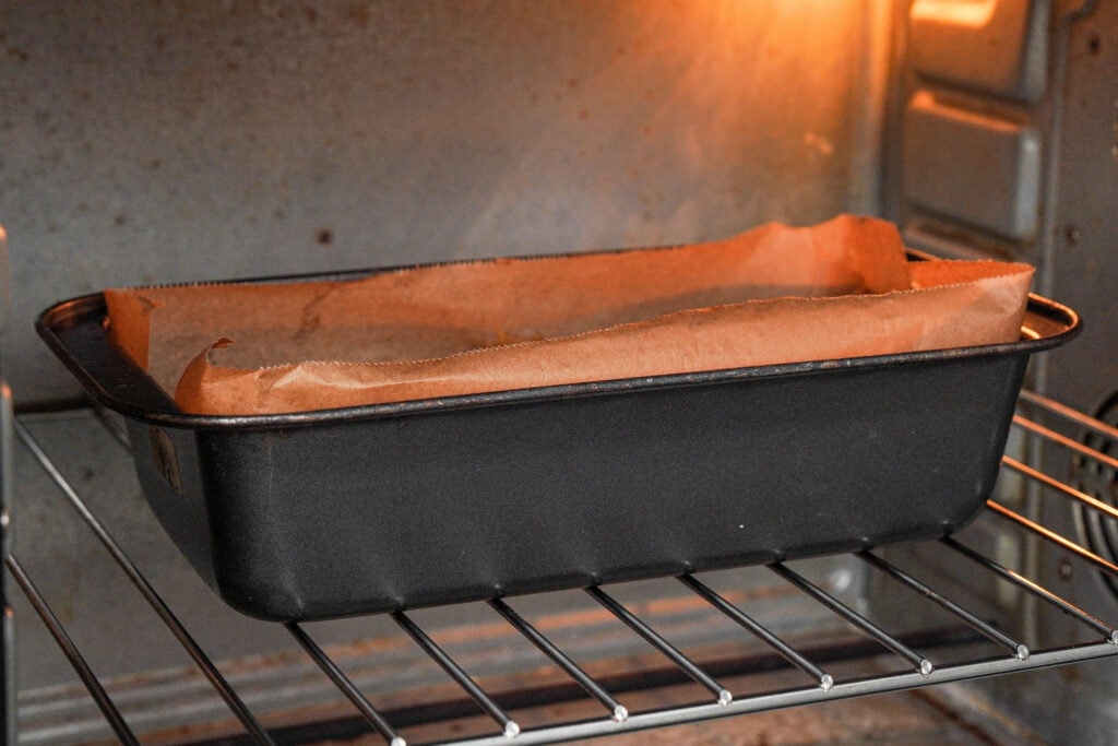 Pumpkin bread in the oven baking. You can see the parchment paper hanging over the sides.