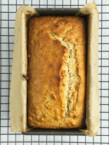 baked loaf of maple walnut bread in the pan cooling on a rack.