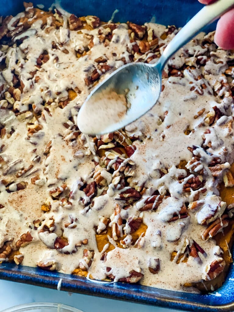 Drizzling melted icing with a spoon on top of the unbaked cake with pecans on top.