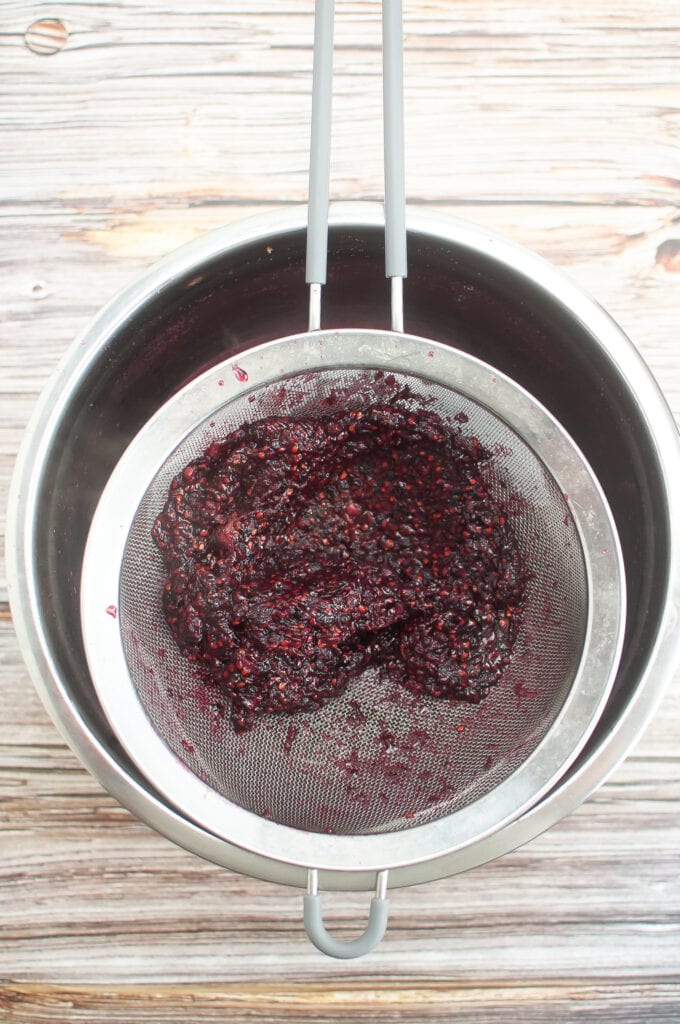 A wire mesh over a pan with blackberry seeds and some pulp. This jam has been pushed through pretty well.