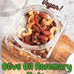 A jar of olive oil rosemary roasted nuts on a wooden cutting board with pinterest text overlay.