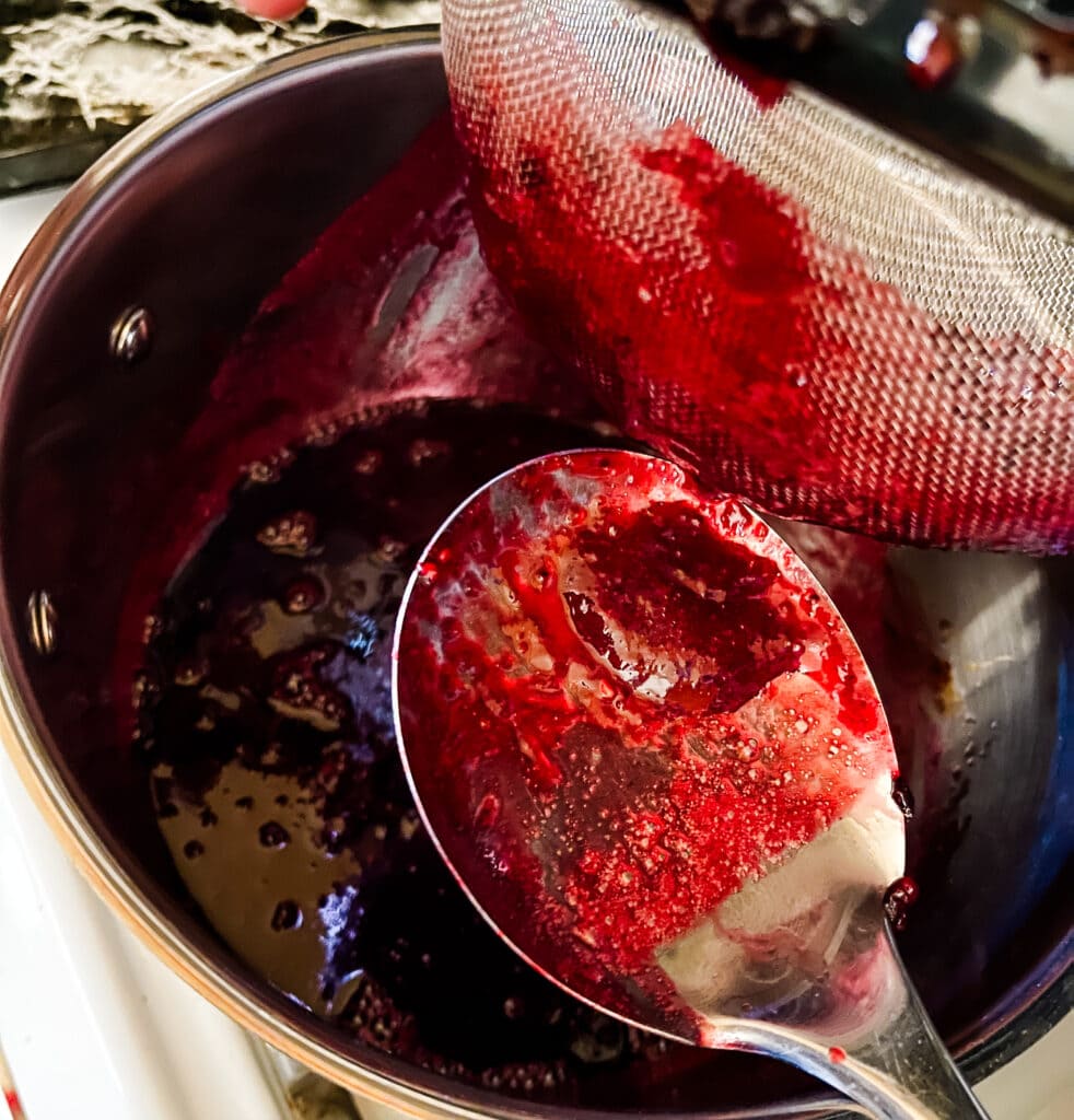 Scraping blackberry jam from the bottom of a mesh strainer holding pulp and seeds.