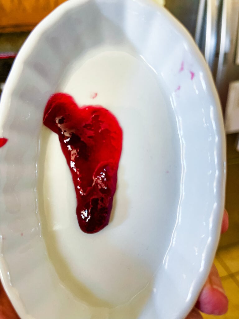 A cold dish out of the freezer with a blob blackberry jam in the middle of it and dripping down showing that it has not cooked enough to gel properly.