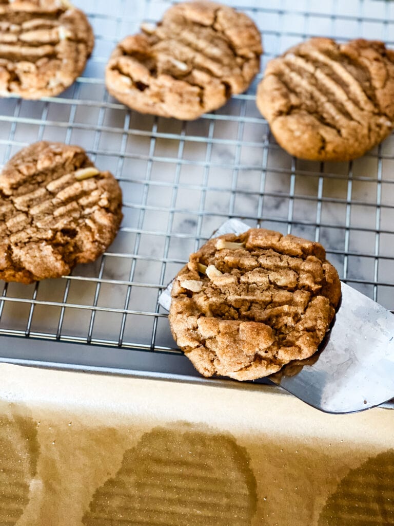 A wire rack holding almond butter cookies with a used parchment paper in front.