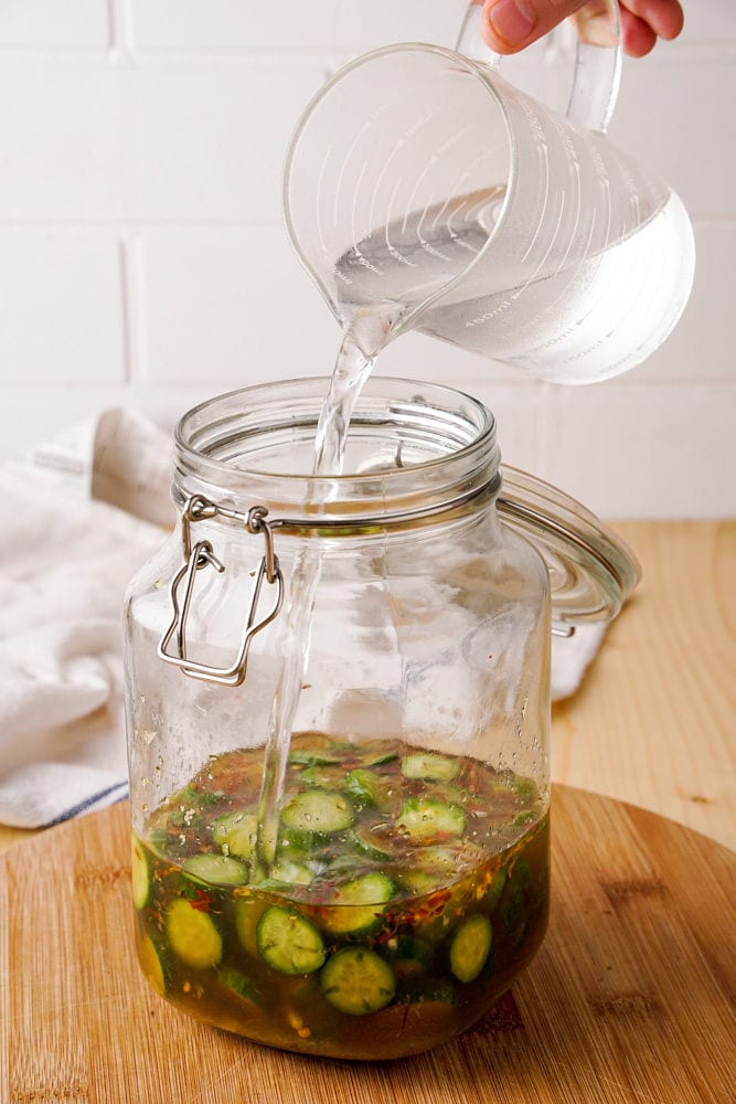 Pouring water into the jar of pickled cucumbers.