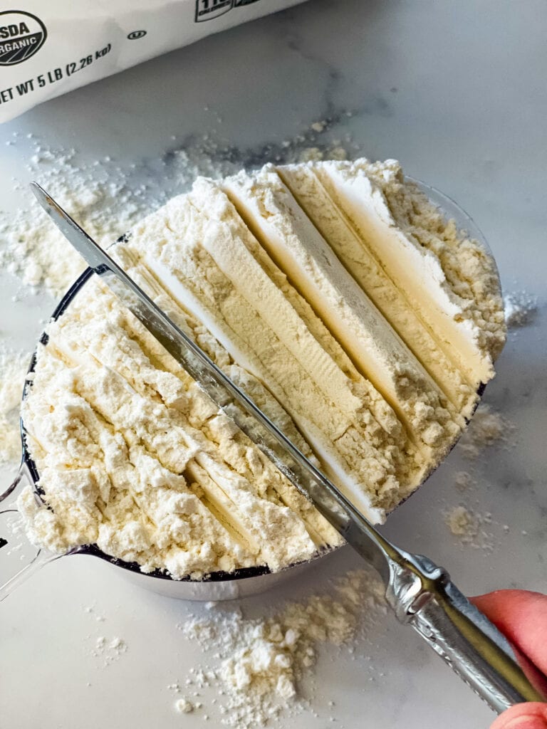 Measuring flour correctly showing cutting the top before swiping the excess.