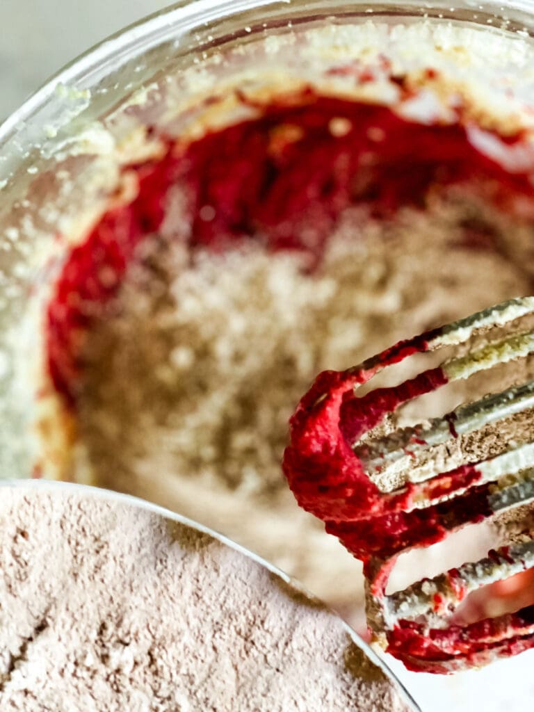 Adding the flour mixture to the wet mixture for red velvet cookies. The beaters are on the right. The bowl of flour on the left.