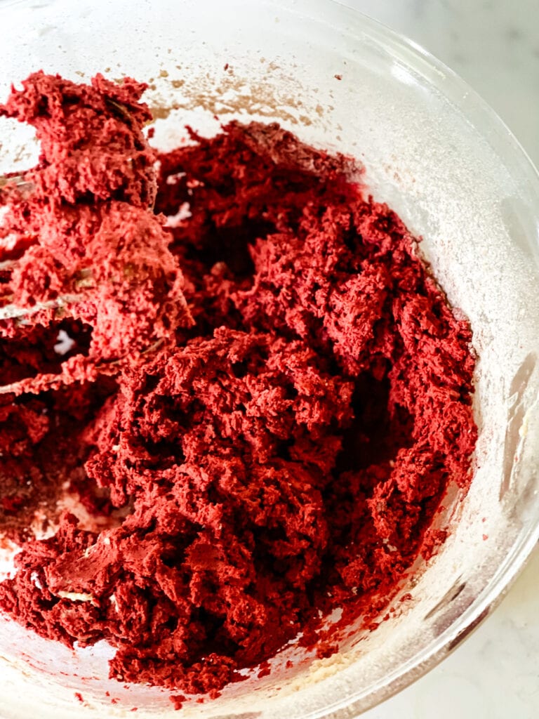 MIxed red velvet cookie dough in a glass bowl with the beaters on the left.