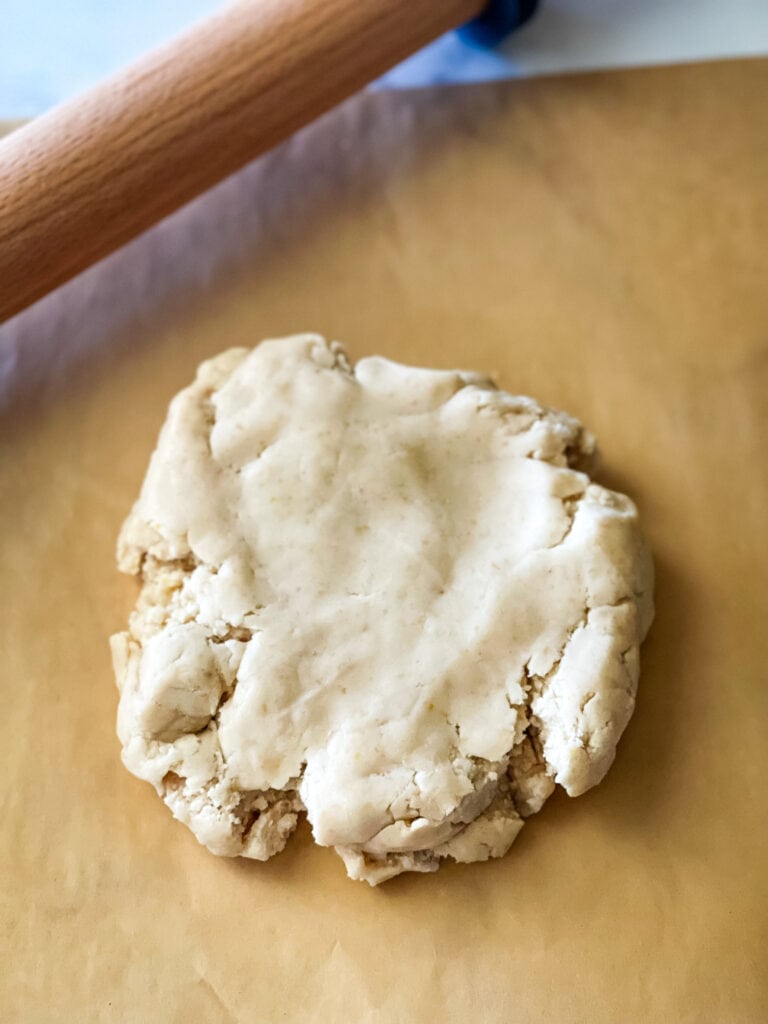 A disc of dough on parchment paper ready to roll. A wooden rolling pin in the top left.