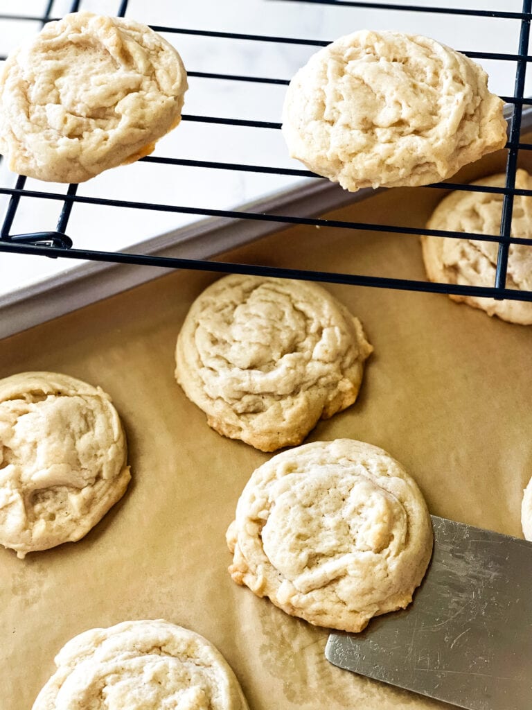 Lifting a sugar cookie from the parchment lined cookie sheet with a rack of sugar cookies at the top.