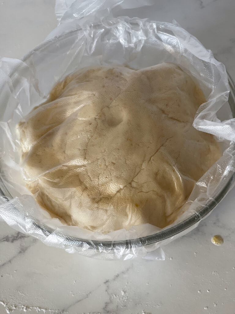 The sugar cookie dough in a glass bowl covered by plastic wrap ready to refrigerate.
