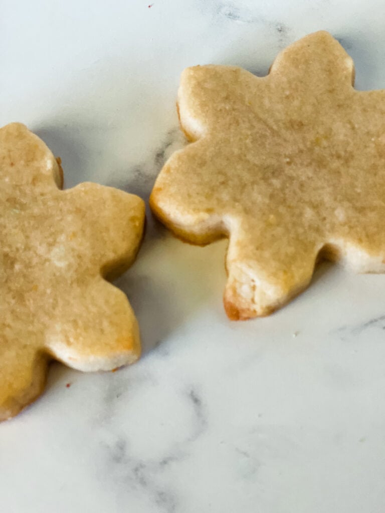 Showing two baked snowflake cookies. The point of this photo is that the cookie on the right has a weird piece that didn't cook out and melt away because the cookies don't spread.
