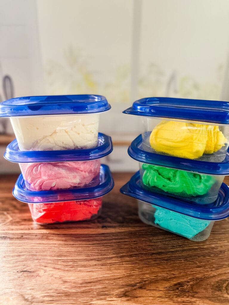 Six little tubs of colored vegan buttercream frosting.
