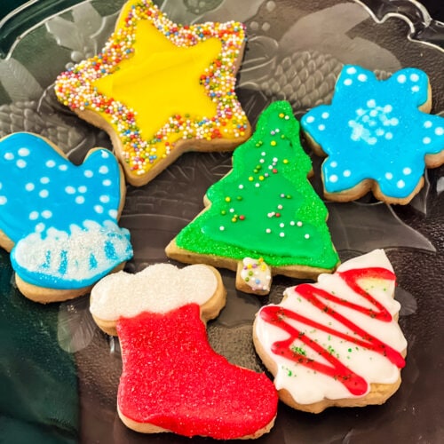 A plate of Christmas cookies iced with vegan icing including a star, two trees, snowflake, mitten, and stocking.