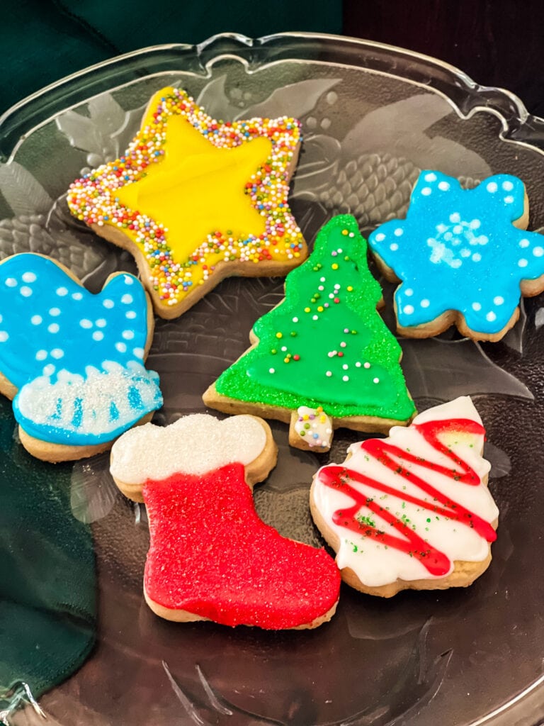 A plate of Christmas cookies iced with vegan icing including a star, two trees, snowflake, mitten, and stocking.