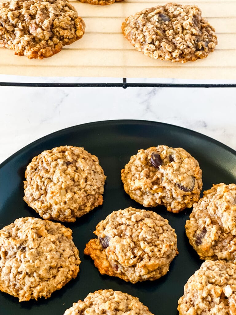 Vegan Banana Oatmeal Cookies on a black plate with a parchment covered cooling rack holding more cookies in the rear.