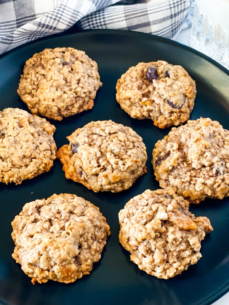 Vegan Banana Oatmeal Cookies on a black plate with a gray checked napkin and glass of plant milk in the rear.